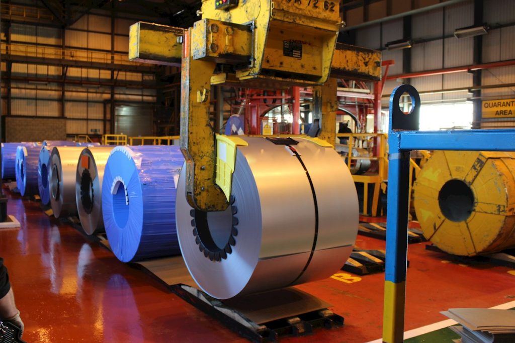 A man is standing next to a large roll of metal.