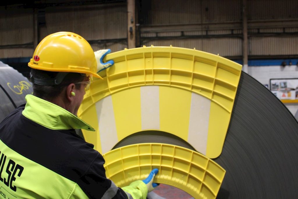 A worker wearing a yellow safety helmet is working on a large metal sheet.