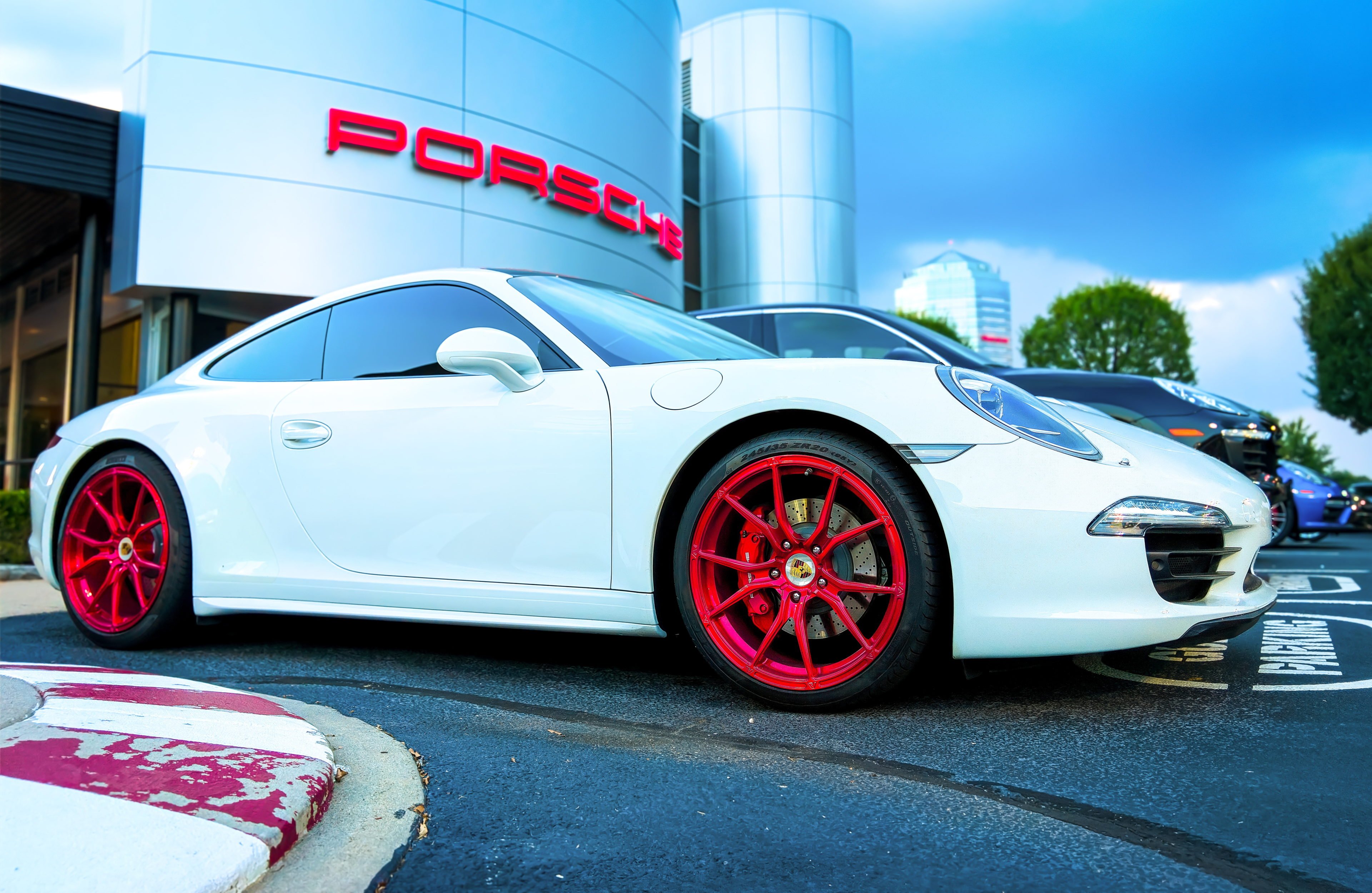 A white porsche 911 parked in front of a porsche dealership.