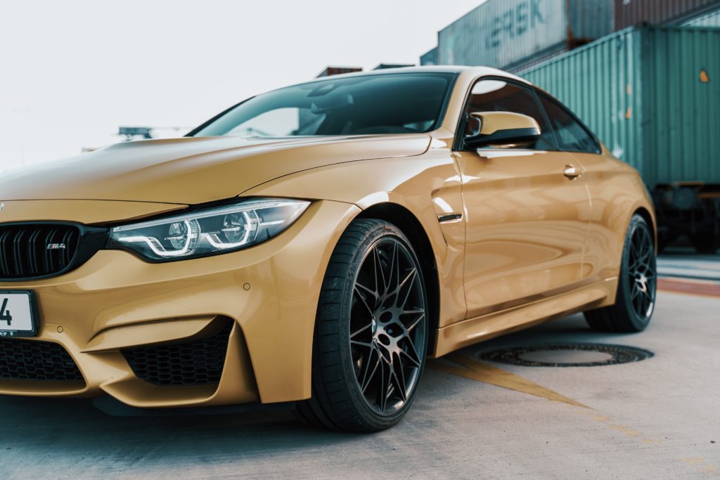 A gold bmw m4 parked in front of a container.
